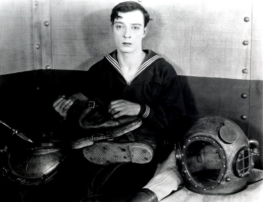 Buster Keaton in a sailor outfit beside a diving helmet in The Navigator