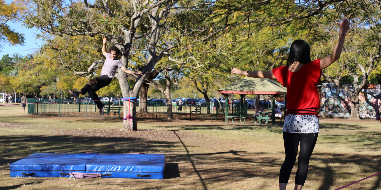 A person walking a slackline between two trees in a park